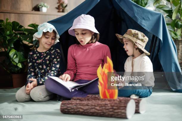 two child girls and one toddler boy playing camping game and reading book at home, concept for activities for activities at home for children - campfire storytelling stock pictures, royalty-free photos & images