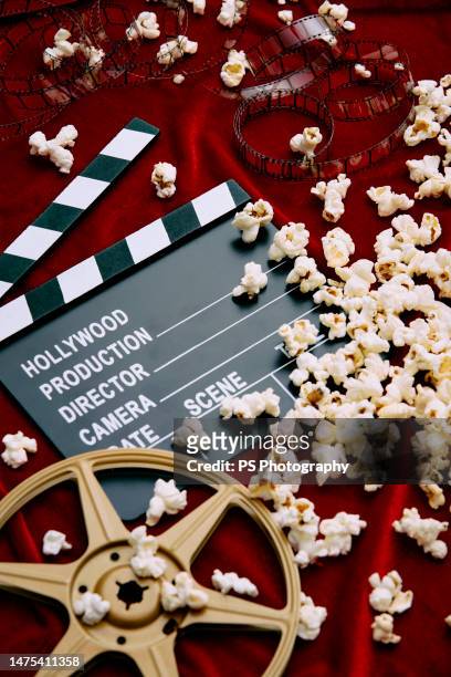 clapperboard, film reel, film and spilled popcorn on red satin background. - red carpet event stock-fotos und bilder