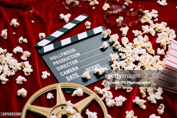 clapperboard, film reel, film and spilled popcorn on red satin background. - hollywood movie stock pictures, royalty-free photos & images