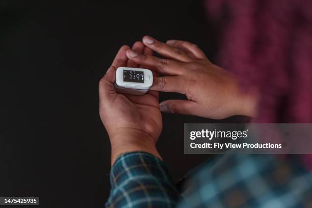 woman checking blood oxygen levels with finger pulse oximeter - anaemia stock pictures, royalty-free photos & images