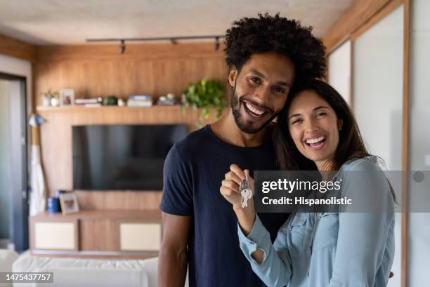 happy couple buying a house and holding the keys while smiling - new house imagens e fotografias de stock