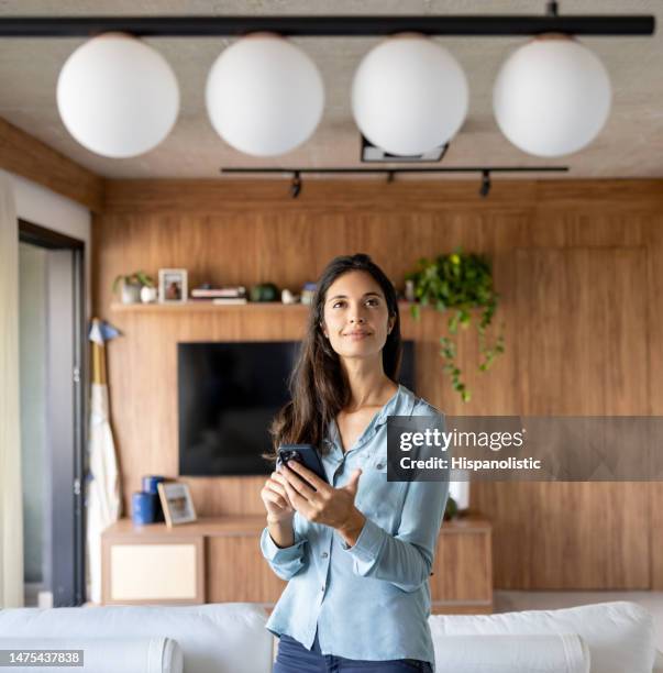 mujer controlando una lámpara en su casa usando un sistema automatizado - interruptor fotografías e imágenes de stock