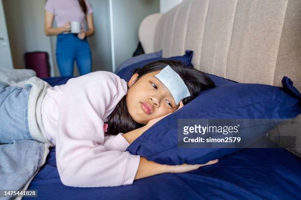 sick asian girl lying in bed with cold compress on her forehead at home - hot body girls stock pictures, royalty-free photos & images