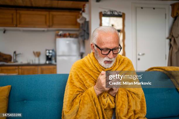 an elderly man wrapped in a blanket is drinking tea, he has a cold - wrapped in a blanket stock pictures, royalty-free photos & images