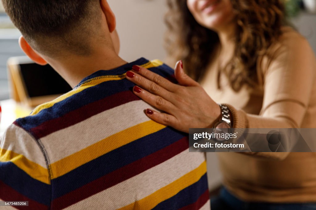 Mother holding hand on her son's shoulder while studying