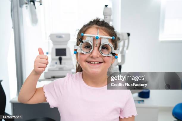 ragazza che mostra il pollice in su mentre indossa il telaio di prova utilizzato per i test della vista, presso la clinica oftalmologica - miopia foto e immagini stock
