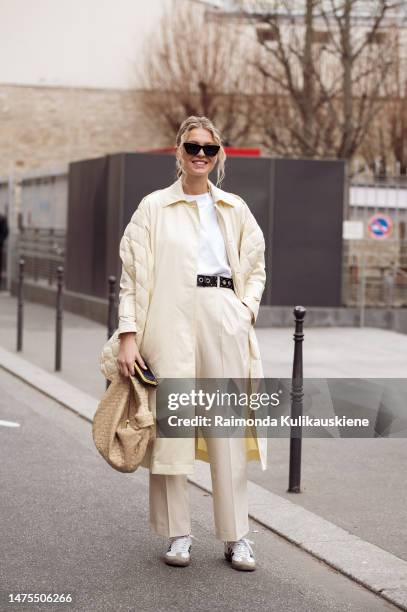 Hollie Mercedes Peters wears a cream trench coat, cream pants, cream puffed Jil Sander scarf, beige Bottega Veneta bag and Adidas sneakers outside...