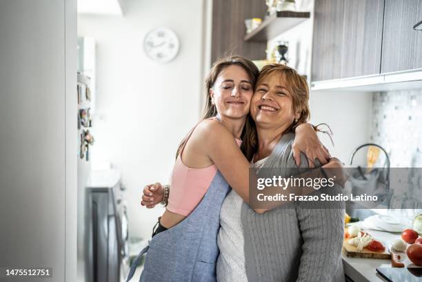 mother and daughter embracing in the kitchen at home - mature adult cooking stock pictures, royalty-free photos & images