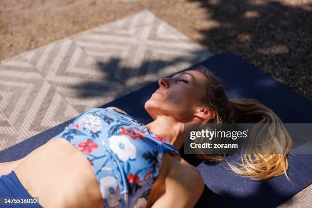 woman resting on mat between exercises outdoors on a sunny day - yoga mat stock pictures, royalty-free photos & images