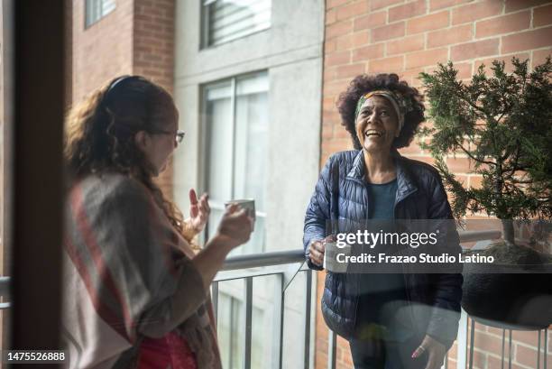 senior friends talking while drinking a coffee cup on the balcony at home - neighbors balcony stock pictures, royalty-free photos & images