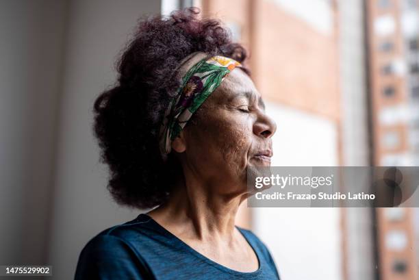 senior woman contemplating with eyes closed at home - senior inhaling stock pictures, royalty-free photos & images