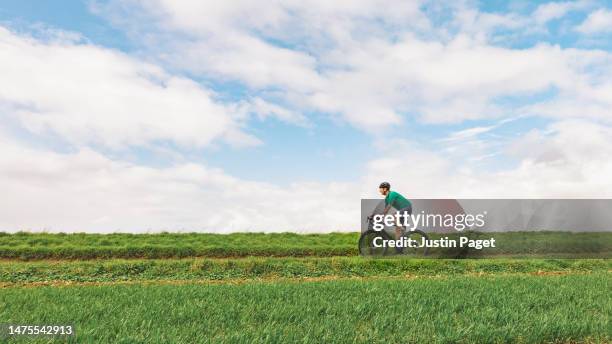 side view of a mature road cyclist against a green foreground and blue sky - strada di campagna foto e immagini stock