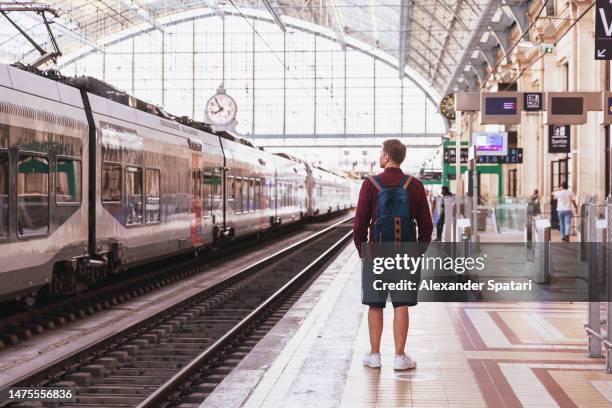 rear view of a man waiting for a train at the train station - estação de metro imagens e fotografias de stock