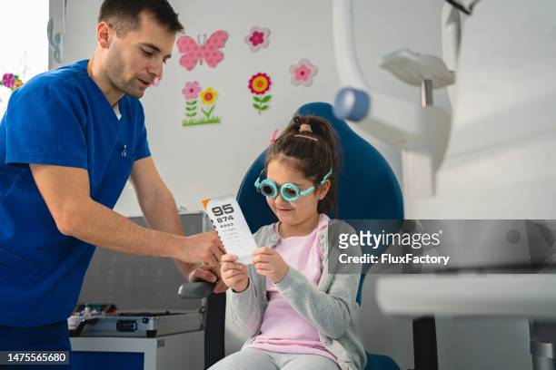 ophthalmologist, examining little girl's eyesight, while using trial frame and different lenses, while she reading snellen chart - ophthalmologist chart stock pictures, royalty-free photos & images
