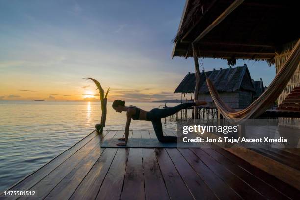 young woman performs yoga moves on dock at sunrise - best performance stock-fotos und bilder