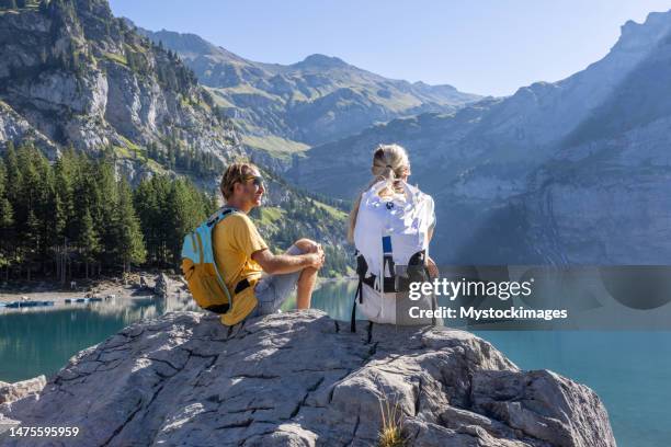 deux randonneurs profitant du magnifique paysage alpin dans les alpes suisses au lever du soleil, ils sont assis sur un rocher au bord du lac - lac-oeschinensee photos et images de collection