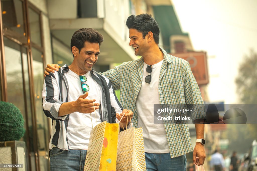 Two happy male friends carrying shopping bags outdoors in city