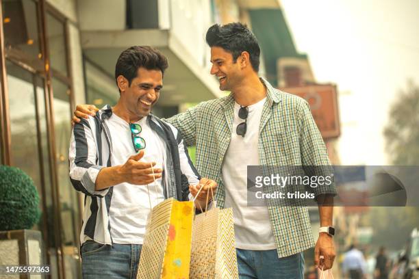 two happy male friends carrying shopping bags outdoors in city - 20s stock pictures, royalty-free photos & images