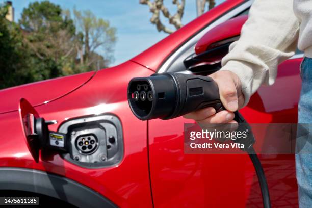 unrecognizable man hand close-up holding an electric plug-in car charger outdoors - red car wire 個照片及圖片檔