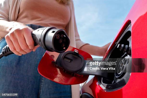 cropped woman hand close-up holding an electric plug-in car charger outdoors - electric car charger imagens e fotografias de stock