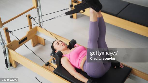 female pilates trainer working out on pilates machine in pilates studio - reformer stock pictures, royalty-free photos & images