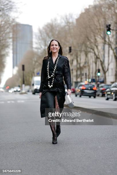 Alba Garavito Torre wears earrings, a long beaded necklace, a black silk trench dress from Elvina Belloir, black floral lace motif fishnet tights...