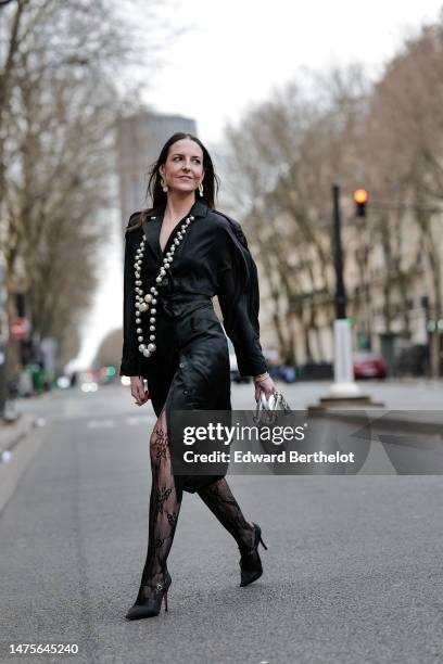 Alba Garavito Torre wears earrings, a long beaded necklace, a black silk trench dress from Elvina Belloir, black floral lace motif fishnet tights...