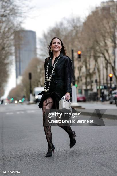 Alba Garavito Torre wears earrings, a long beaded necklace, a black silk trench dress from Elvina Belloir, black floral lace motif fishnet tights...