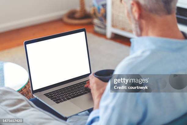 mature man using a blank screen laptop at home. - computer screen over shoulder stock pictures, royalty-free photos & images