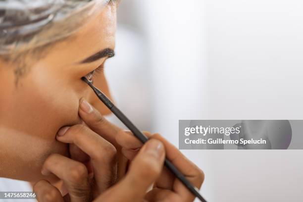 male, applying black eyeliner to her eyes in detail. - delineador fotografías e imágenes de stock