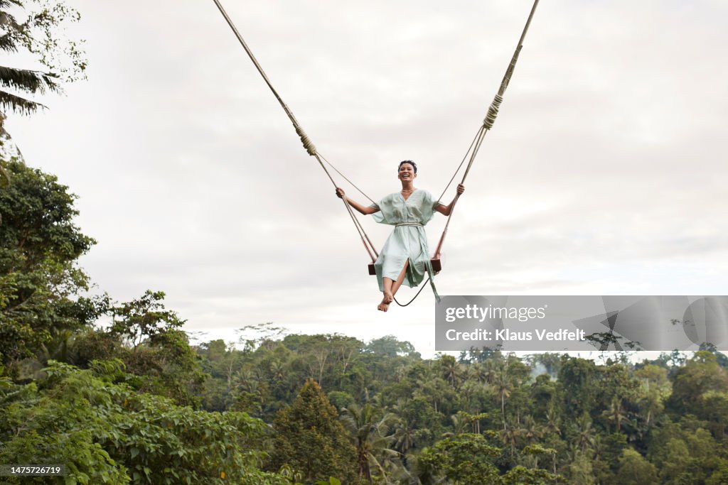Smiling woman on swing over forest