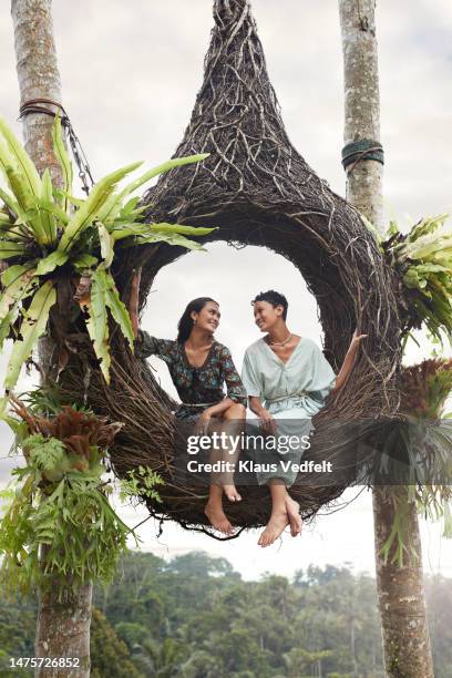 young female friends sitting in nest swing - legs crossed at knee stock pictures, royalty-free photos & images