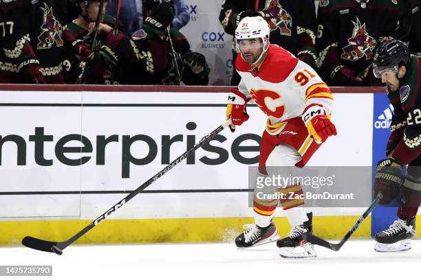 Nazem Kadri of the Calgary Flames skates with the puck against Jack McBain of the Arizona Coyotes at Mullett Arena on March 14, 2023 in Tempe,...