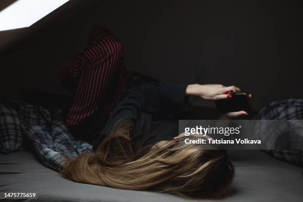 teenage girl 16 years old lying on bed in attic holding phone in her hands spending time on internet in bedroom under window - 12 13 years old girls stock-fotos und bilder