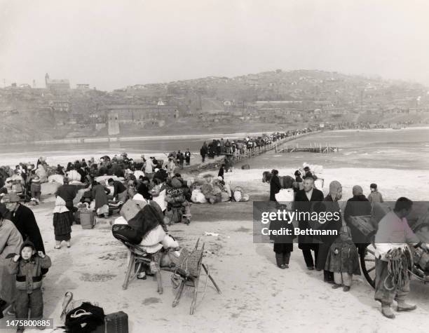 Korean war refugees cross the Han River on a small footbridge as they flee southward from the advancing Chinese and North Korean forces on January...