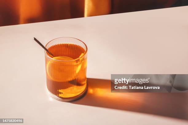 tea with lemons in transparent glass against orange curtains background with beautiful illuminated shadow and copy space. closeup of natural hot beverage. front view, high angle. - tea stock pictures, royalty-free photos & images