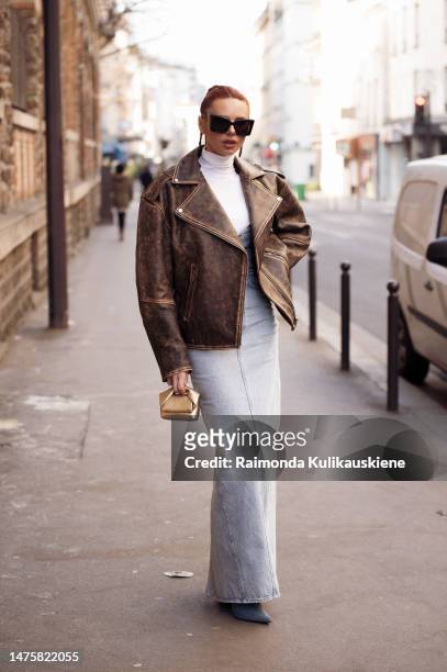 Evelyn Kazantzoglou wears YSL golden bag, brown leather jacket, white turtle neck shirt, high waisted long maxi blue denim skirt or dress outside...