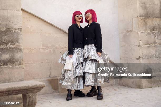 Ami and Aya Amiaya with pink hair wears sunglasses with rhinestones, a silver pearls necklace, a silver shiny ruffled long dress, a black belted...