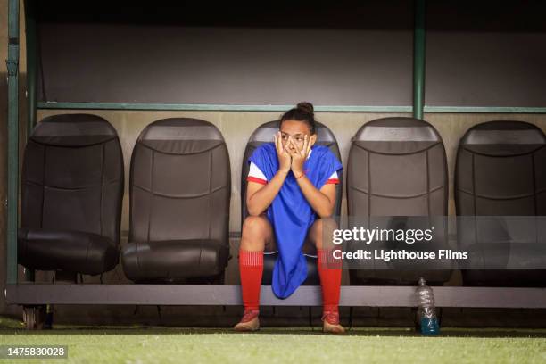 a single professional athlete covers her face in disappointment while sitting on the bench. - banco asiento fotografías e imágenes de stock