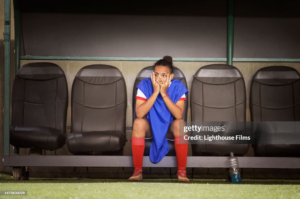 A single professional athlete covers her face in disappointment while sitting on the bench.