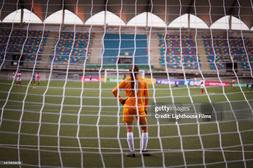 Young professional women's soccer goalie stares out into an empty stadium.