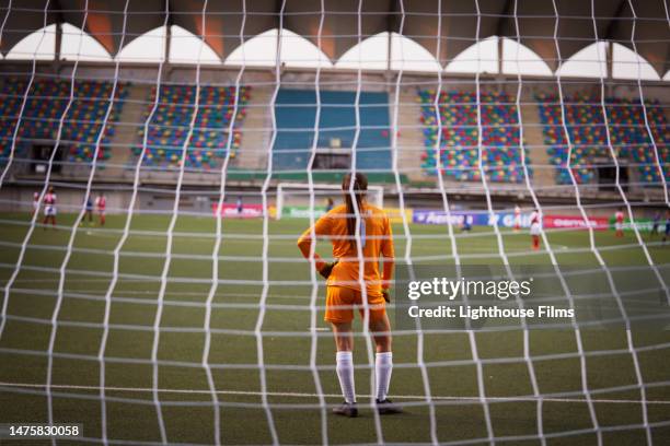 young professional women's soccer goalie stares out into an empty stadium. - woman goalie stock pictures, royalty-free photos & images