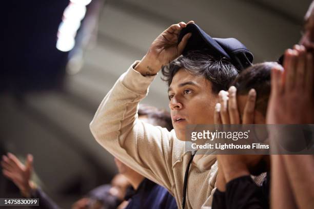 a young man lifts his hat off of his head in disbelief after witnessing a play on the sports field. - expression stress stockfoto's en -beelden