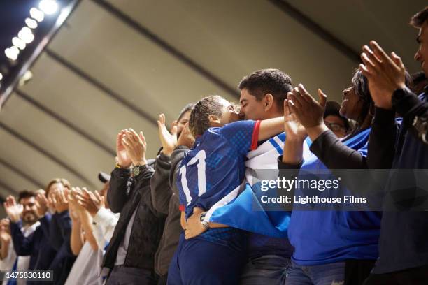 a female athlete leans in and kisses her partner as the partner hugs her waist. - kiss viewer stock pictures, royalty-free photos & images