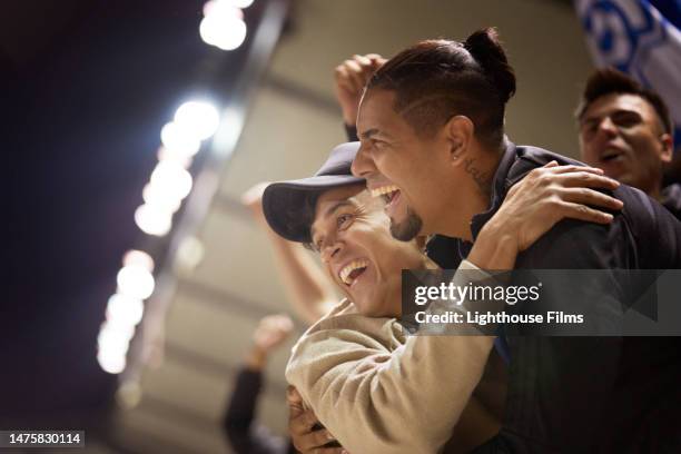 two excited sports fans hug one another after a winning play. - fan stock-fotos und bilder