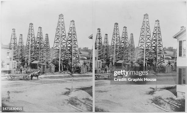 Stereoscopic image showing a man standing on a horse-drawn cart with oil derricks in the background at an oil field, United States, circa 1900.