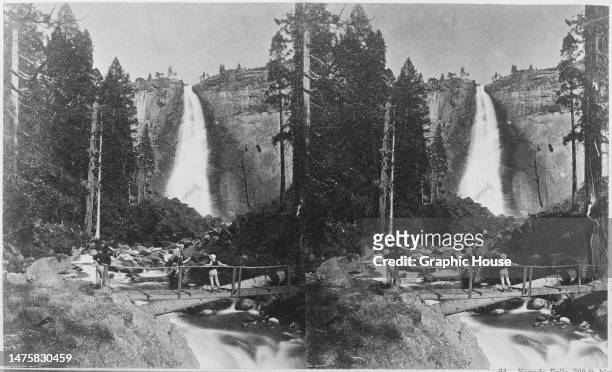 Stereoscopic image showing two people standing on a bridge to admire the Nevada Fall, a 594-foot high waterfall on the Merced River in Yosemite...