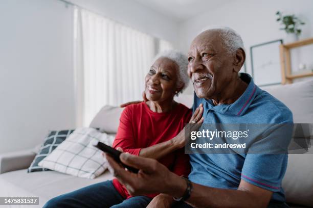 portrait of elderly couple at home watching tv in living room - couple on sofa stock pictures, royalty-free photos & images