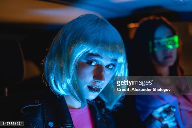 female group portrait of two women who using eyeglasses for virtual reality in car. neon light concept photography, futuristic photo with multi-color lighting indoors the vehicle. girl and neural networks, people and technology for communication. - cyber punk girl stock pictures, royalty-free photos & images