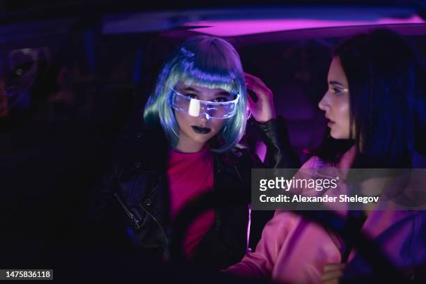 female group portrait of two women who using eyeglasses for virtual reality in car. neon light concept photography, futuristic photo with multi-color lighting indoors the vehicle. girl and neural networks, people and technology for communication. - cyber punk girl stock pictures, royalty-free photos & images